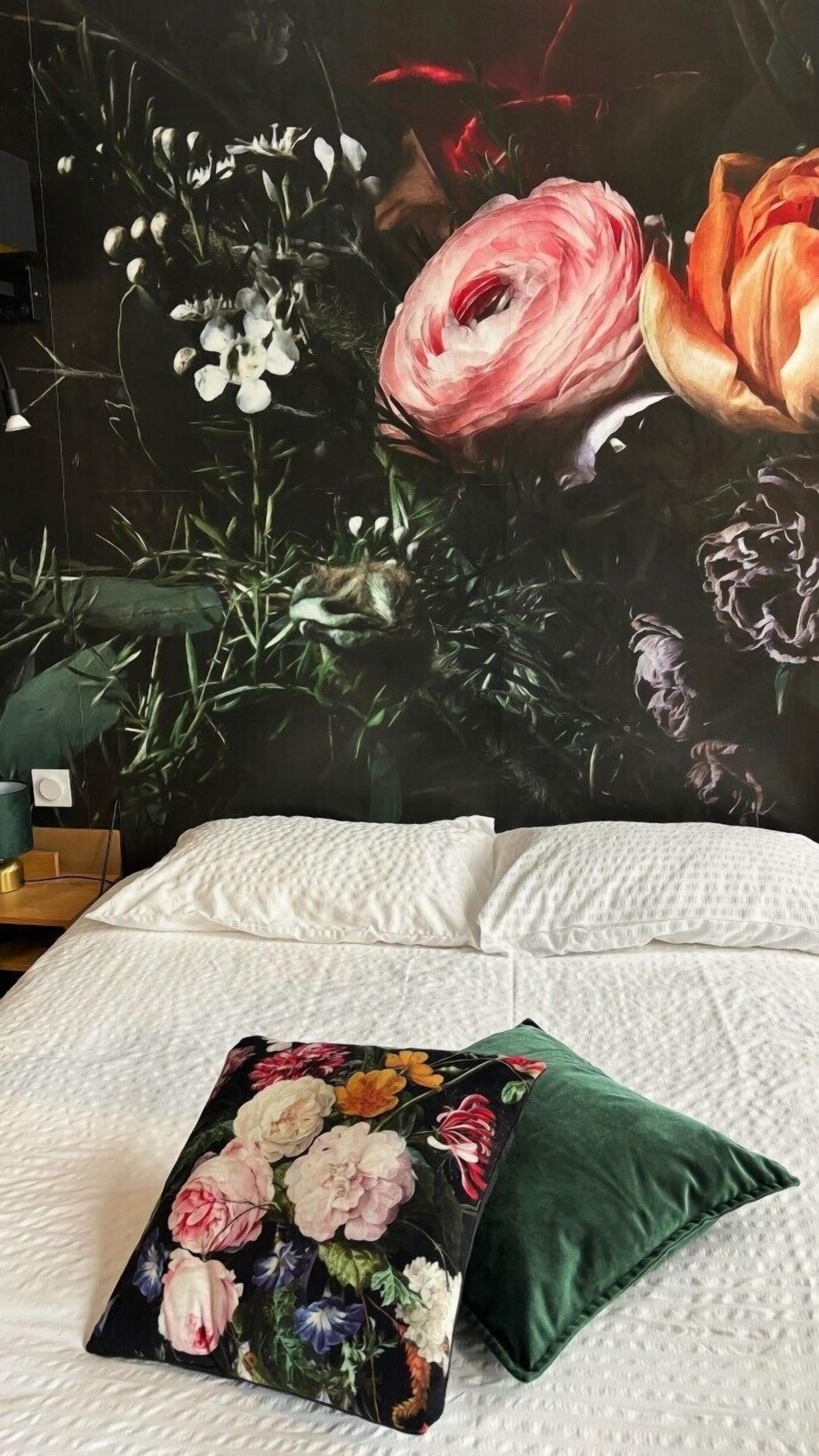 A bed with a white textured cover, a green pillow, and a floral pillow.
