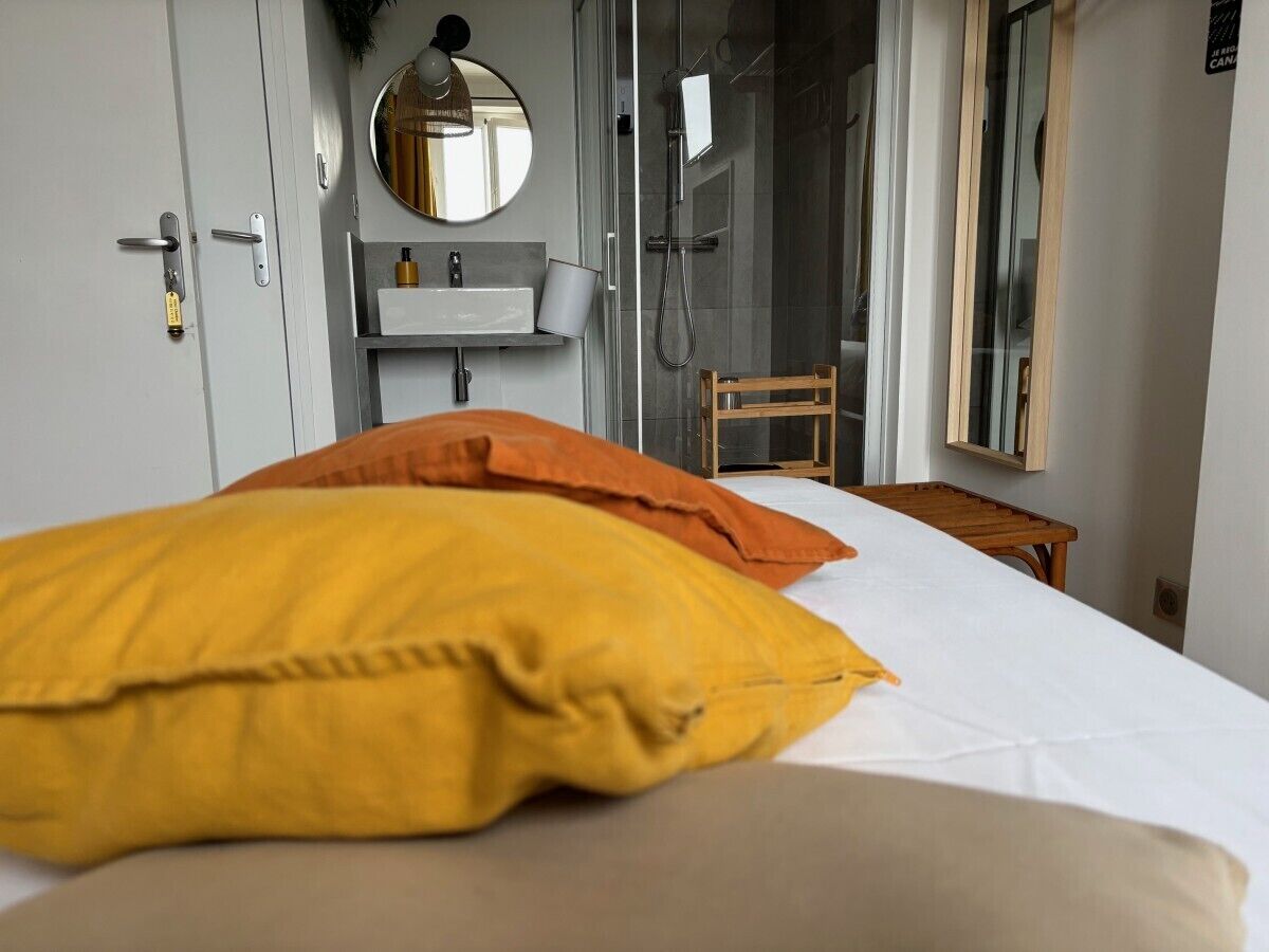 Un dormitorio con cama, almohadas, mesita de noche, espejo, lavabo y zona de ducha.