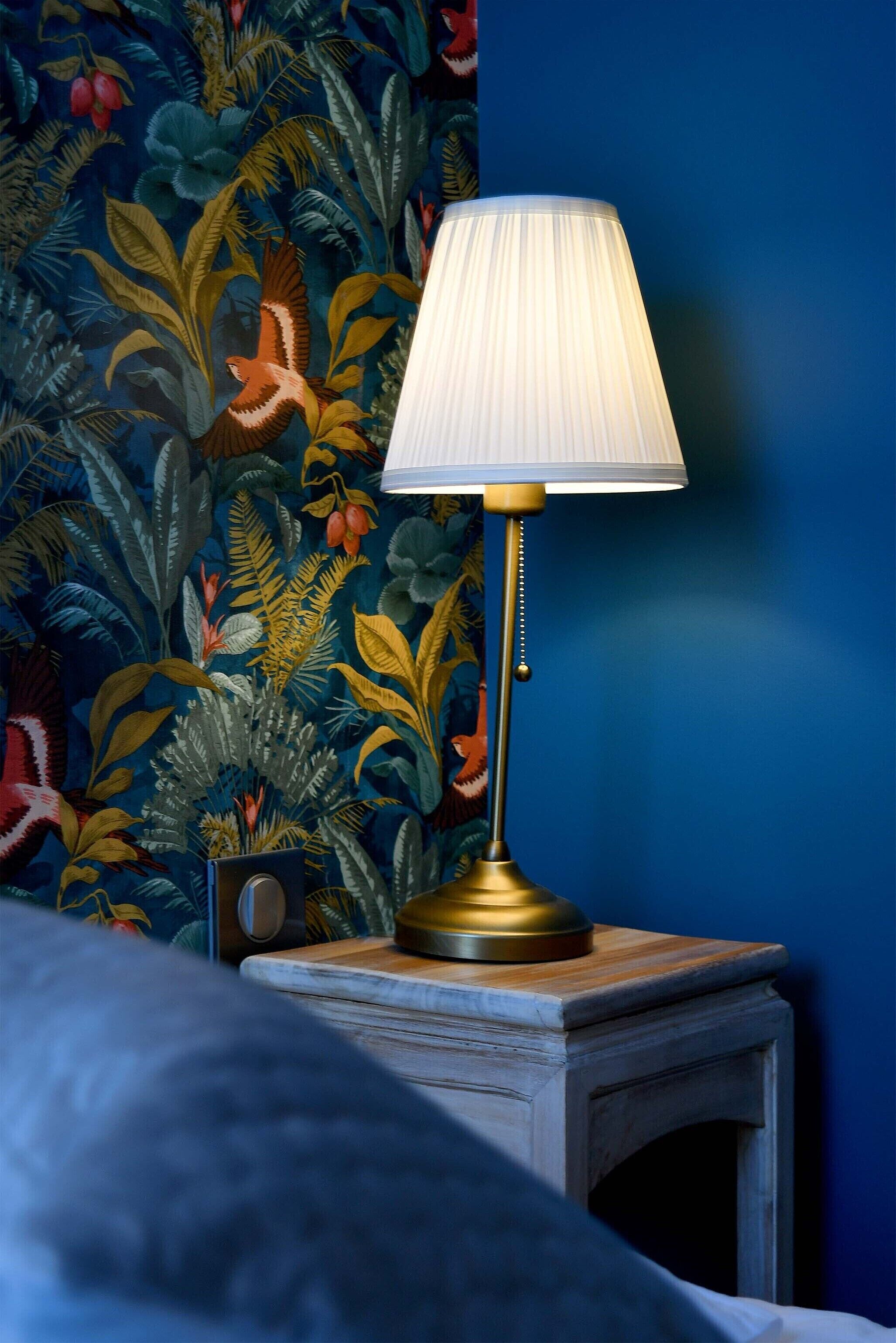 A lamp on a bedside table with a floral wallpaper background.