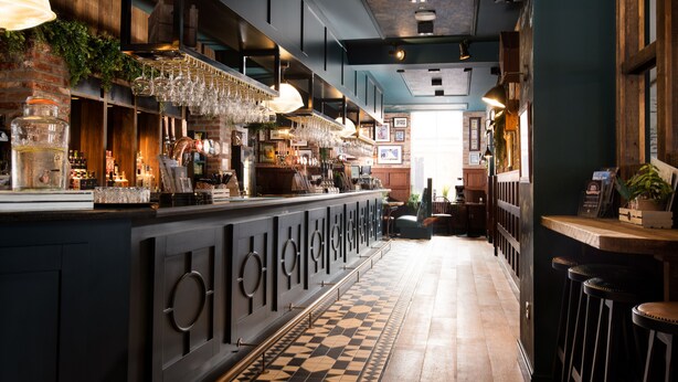 A bar area with a long counter, hanging glasses, and a patterned floor. - The Northallerton Inn - The Inn Collection Group (Northallerton)