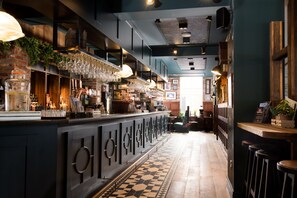 Una zona de bar con una barra larga, copas colgantes y un suelo estampado.