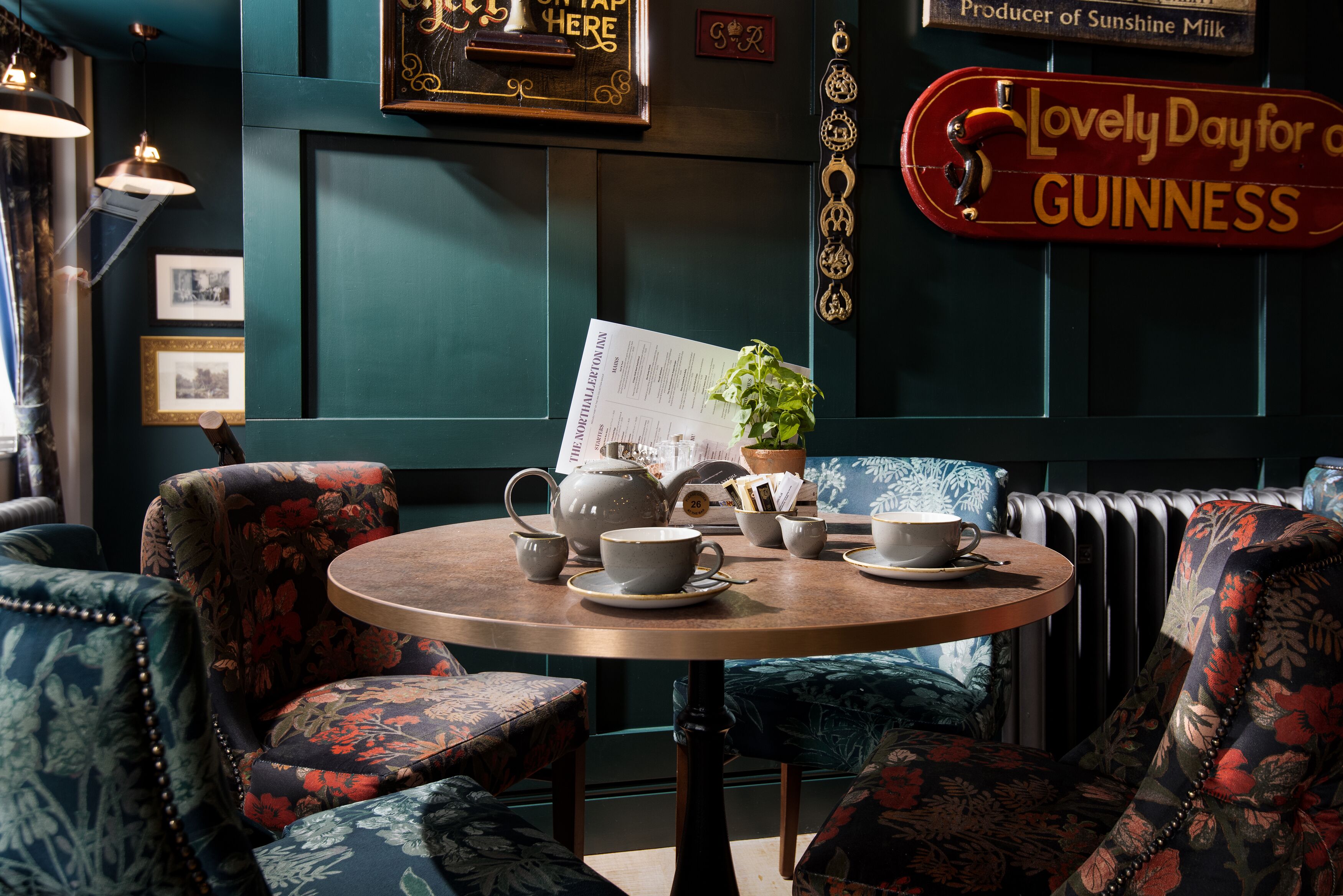 A cozy seating area with floral upholstery, a wooden table with tea set, and vintage decor including a sign for Guinness.