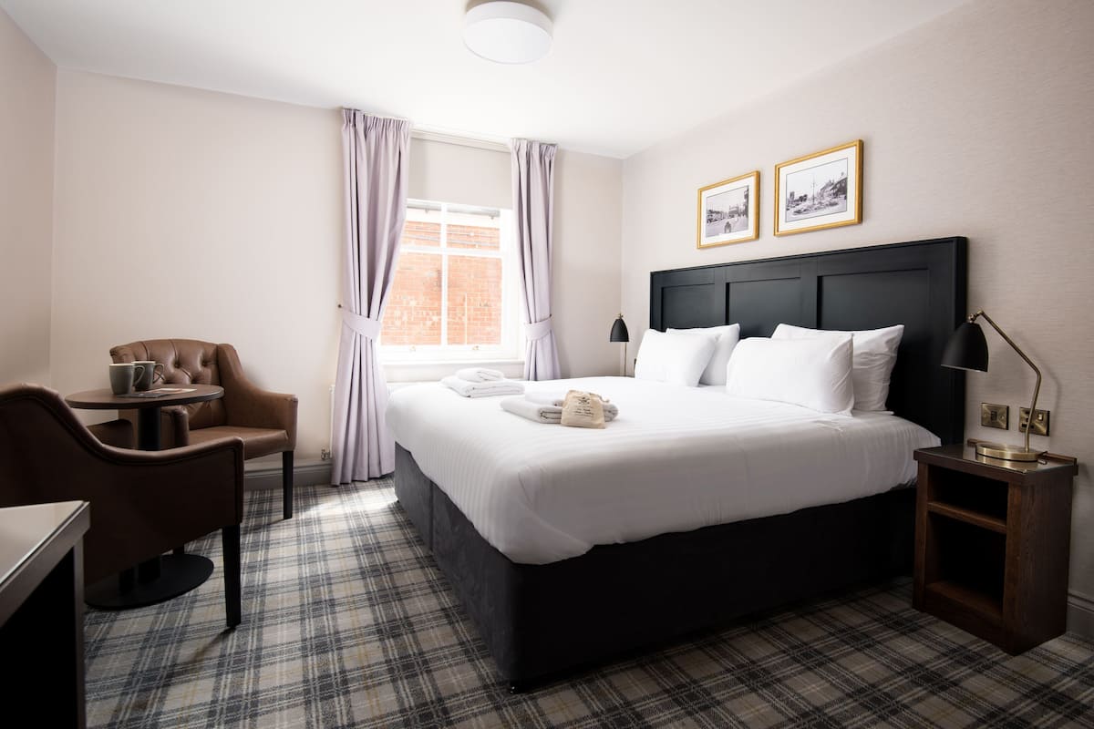 A hotel room with a large bed, a chair, a small table, and a nightstand.