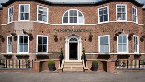 A brick building with a sign reading "The Northallerton Inn." It features a central entrance with steps, multiple windows, and flower boxes on the ground floor. - The Northallerton Inn - The Inn Collection Group (Northallerton)