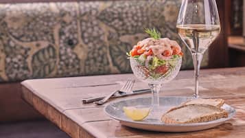 A dining table with a glass salad bowl, a glass of white wine, and a slice of bread on a plate.