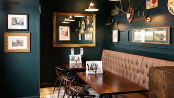 A restaurant interior with dark walls, framed pictures, a large mirror, and a leather booth.