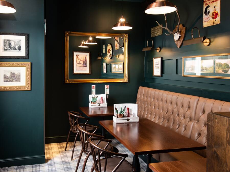 A restaurant interior with dark walls, framed pictures, a large mirror, and a leather booth.