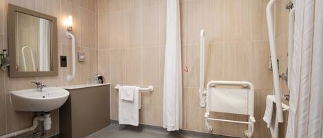 A modern bathroom with a sink, mirror, shower, and grab bars.