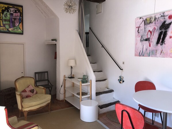 Una stanza con una scala, una sedia, un tavolo e una lampada.