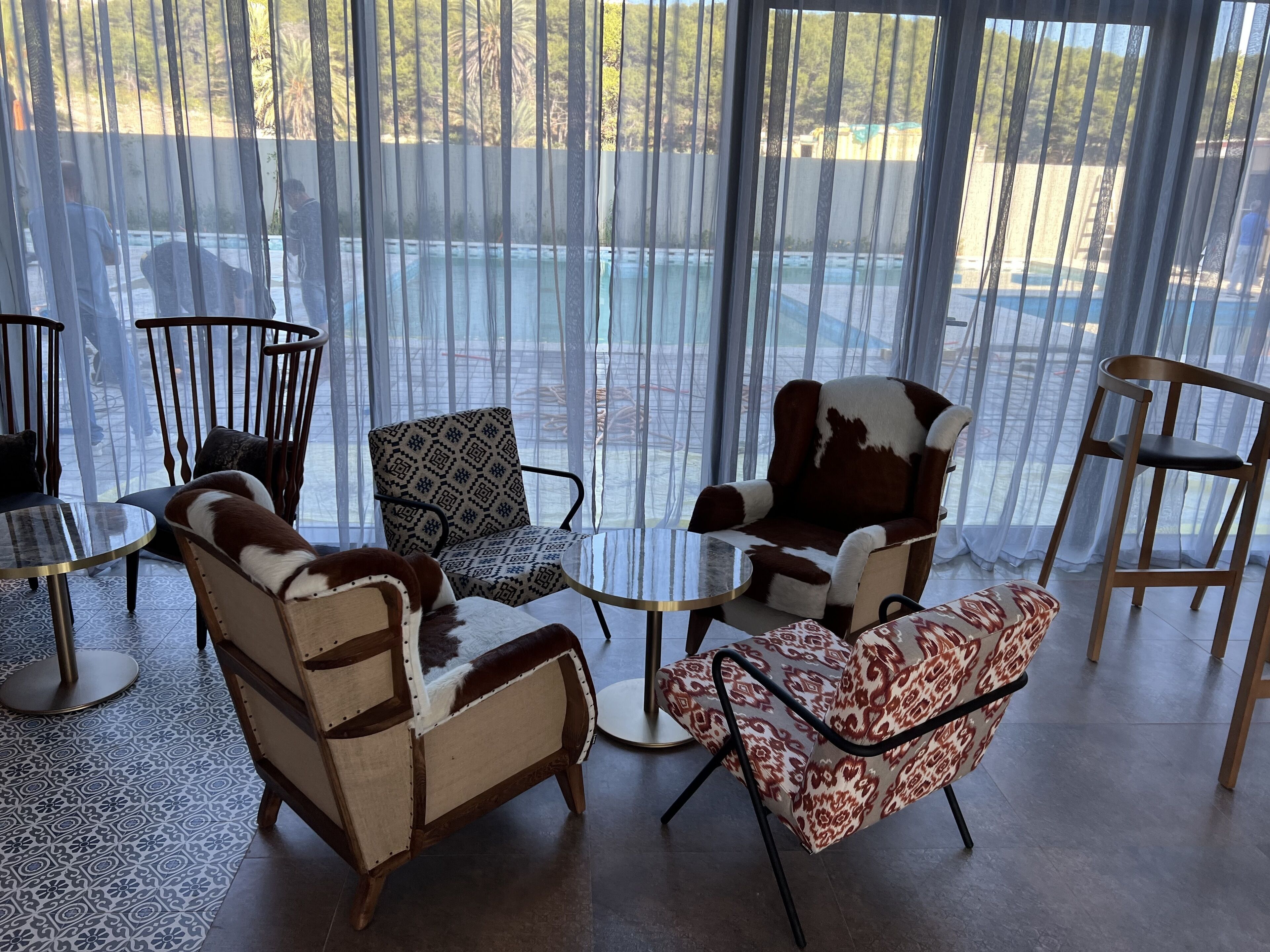 A room with a view of a pool, featuring a mix of patterned and animal print chairs, a small round table, and a patterned rug.