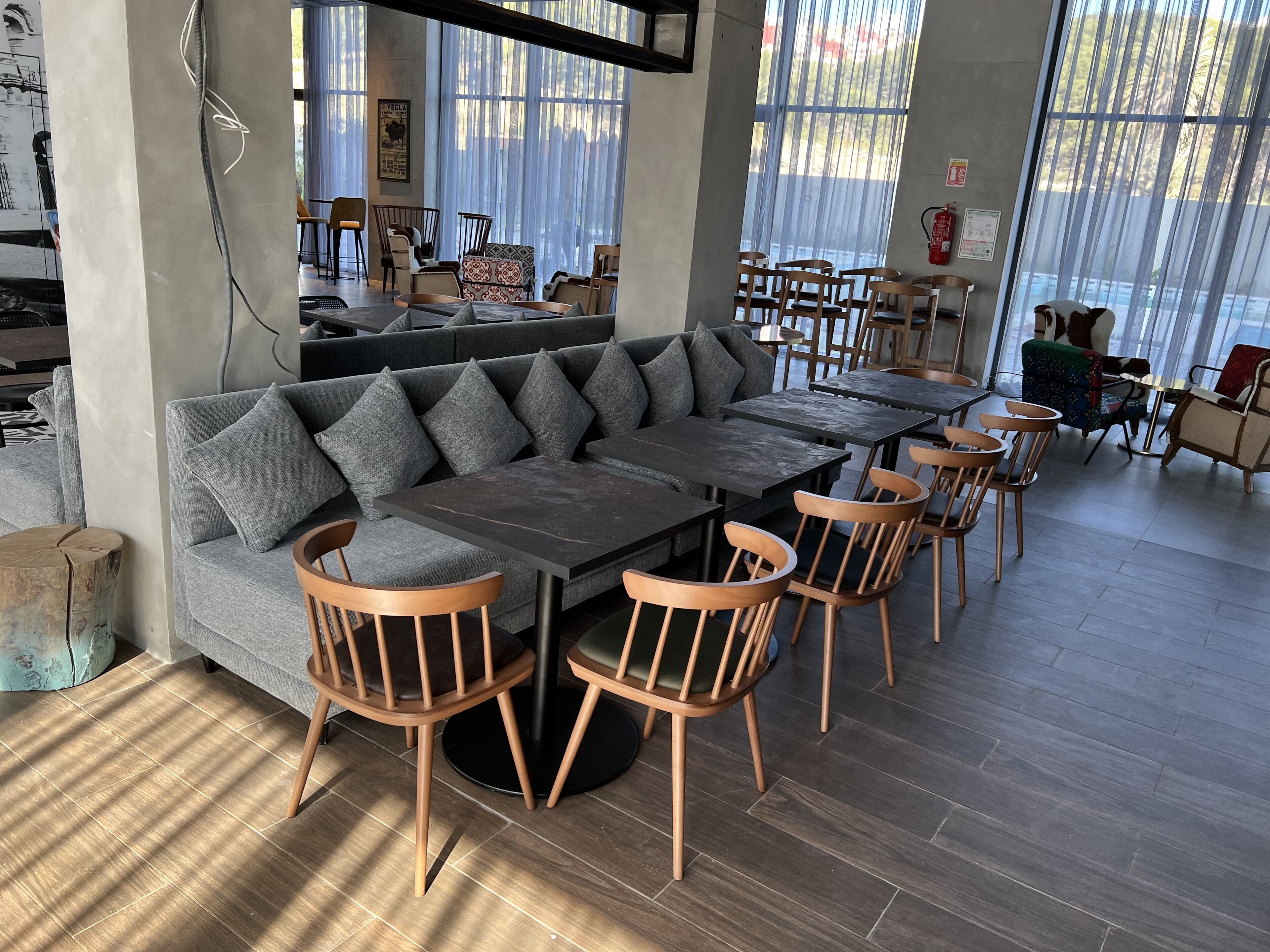 A modern cafe with a grey sofa, wooden chairs, and a large table.