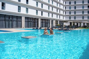 Um hotel moderno com uma grande piscina interior, espreguiçadeiras e um edifício alto com amplas janelas.