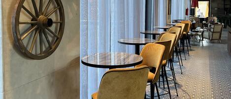 A long corridor with tables and chairs, large windows with sheer curtains, and decorative wall elements.
