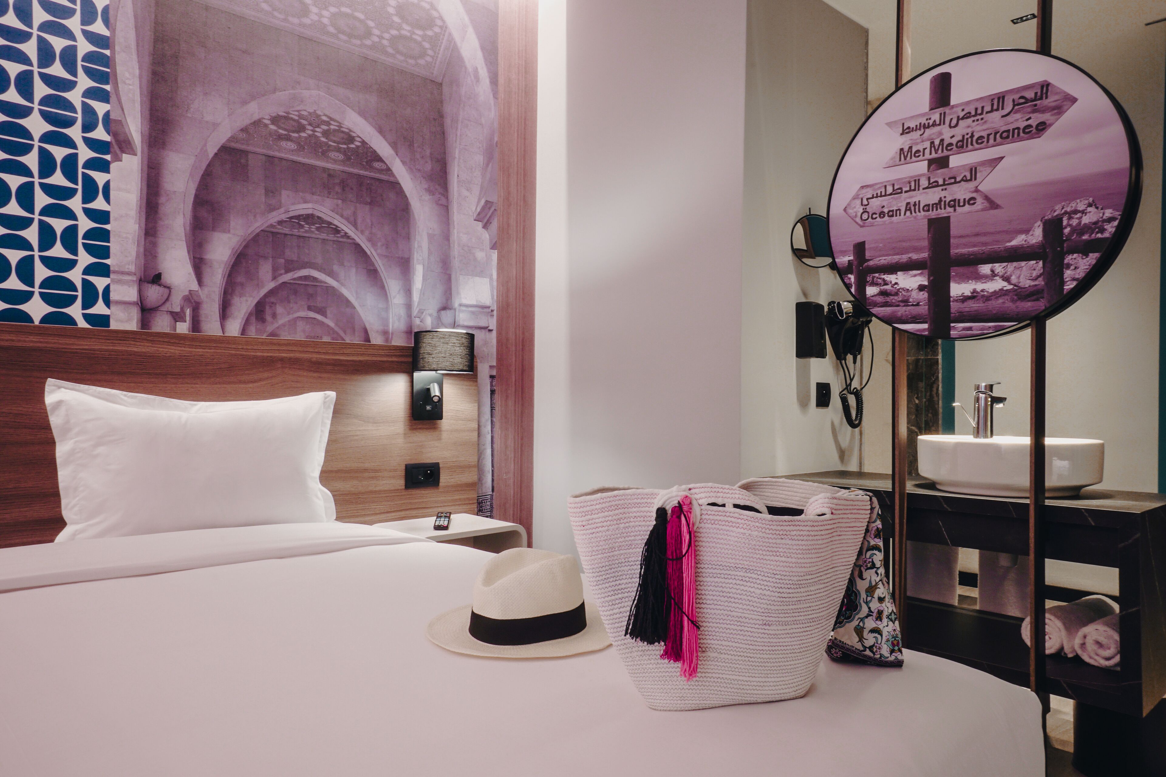 A hotel room with a bed, a large mirror, a wall-mounted phone, and a decorative wall with arches.
