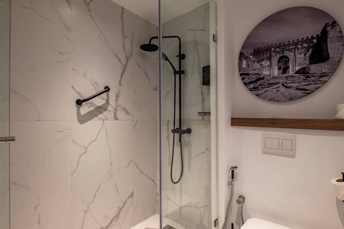 A modern bathroom with a glass-enclosed shower, marble walls, and a circular wall-mounted picture of a historical building.