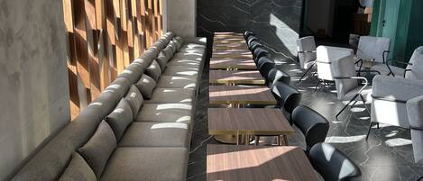 Un área de lounge moderna con un largo banco y mesas, suelo de mármol y un revestimiento de pared de madera.