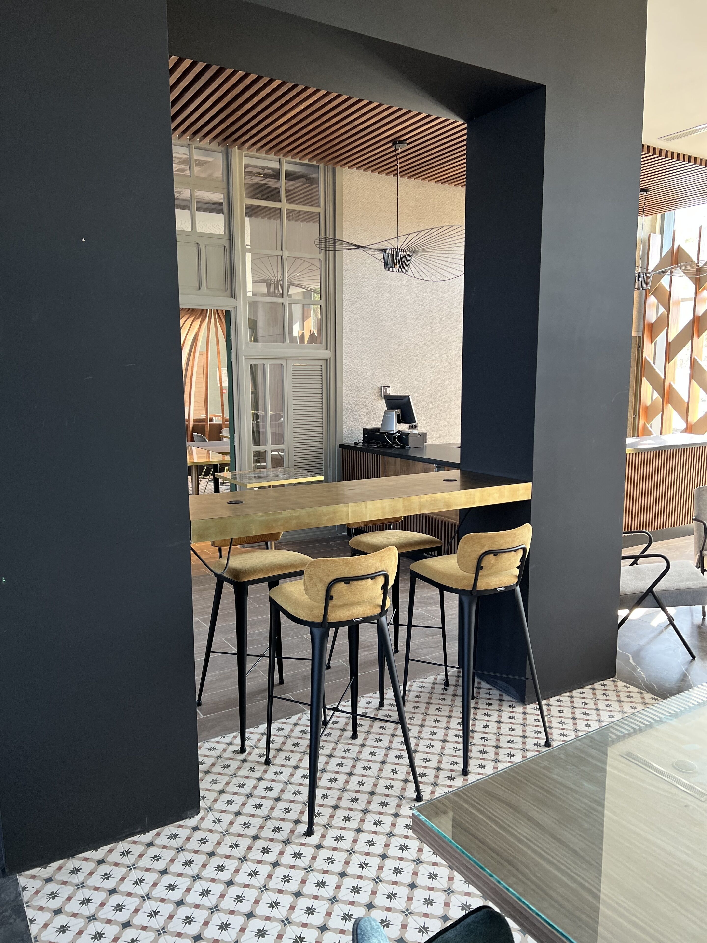 Un espace de repas moderne avec une longue table en bois et des chaises assorties, un sol à motifs et une vue sur l’extérieur grâce à une grande fenêtre.