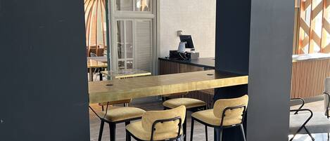 Un espace de repas moderne avec une longue table en bois et des chaises assorties, un sol à motifs et une vue sur l’extérieur grâce à une grande fenêtre.