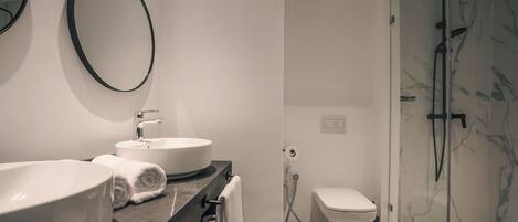 A modern bathroom with a large oval sink, a round mirror, a toilet, and a glass-enclosed shower area.