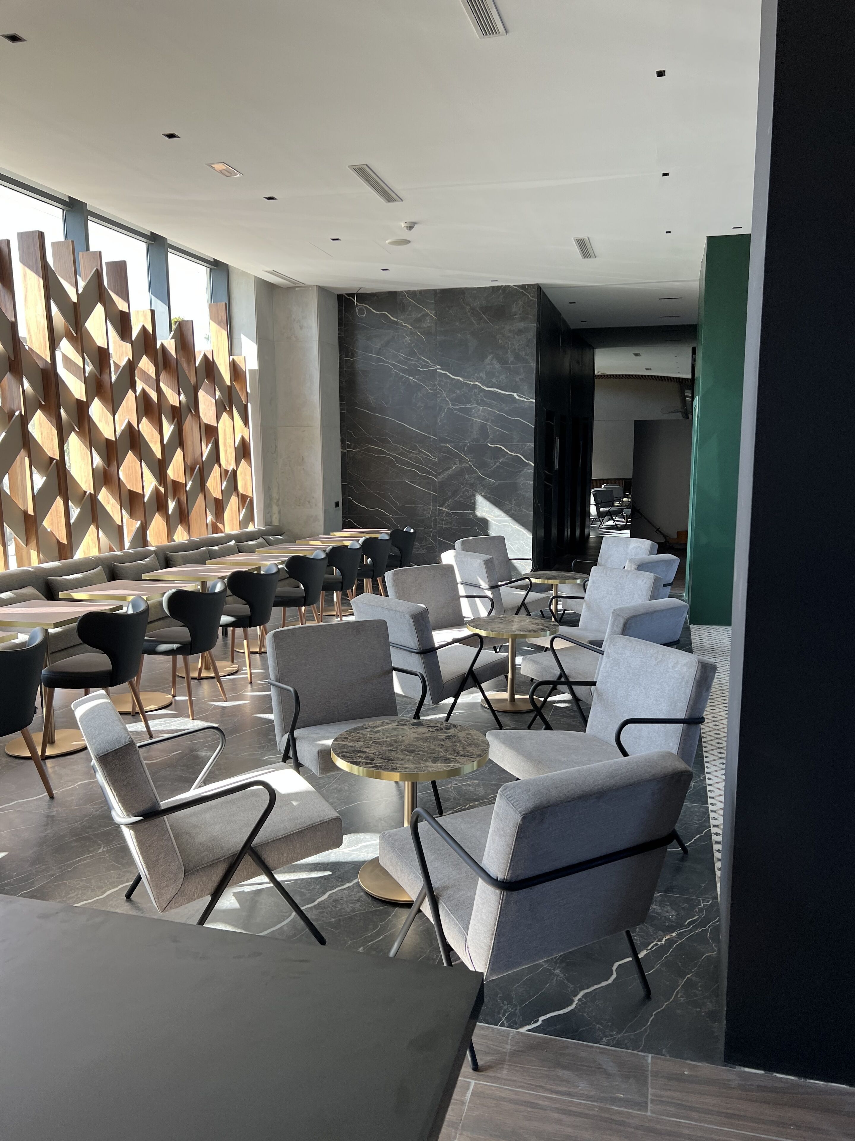 Een moderne lounge met zitplaatsen en tafels, marmeren muren en een geometrisch houten roomdivider.
