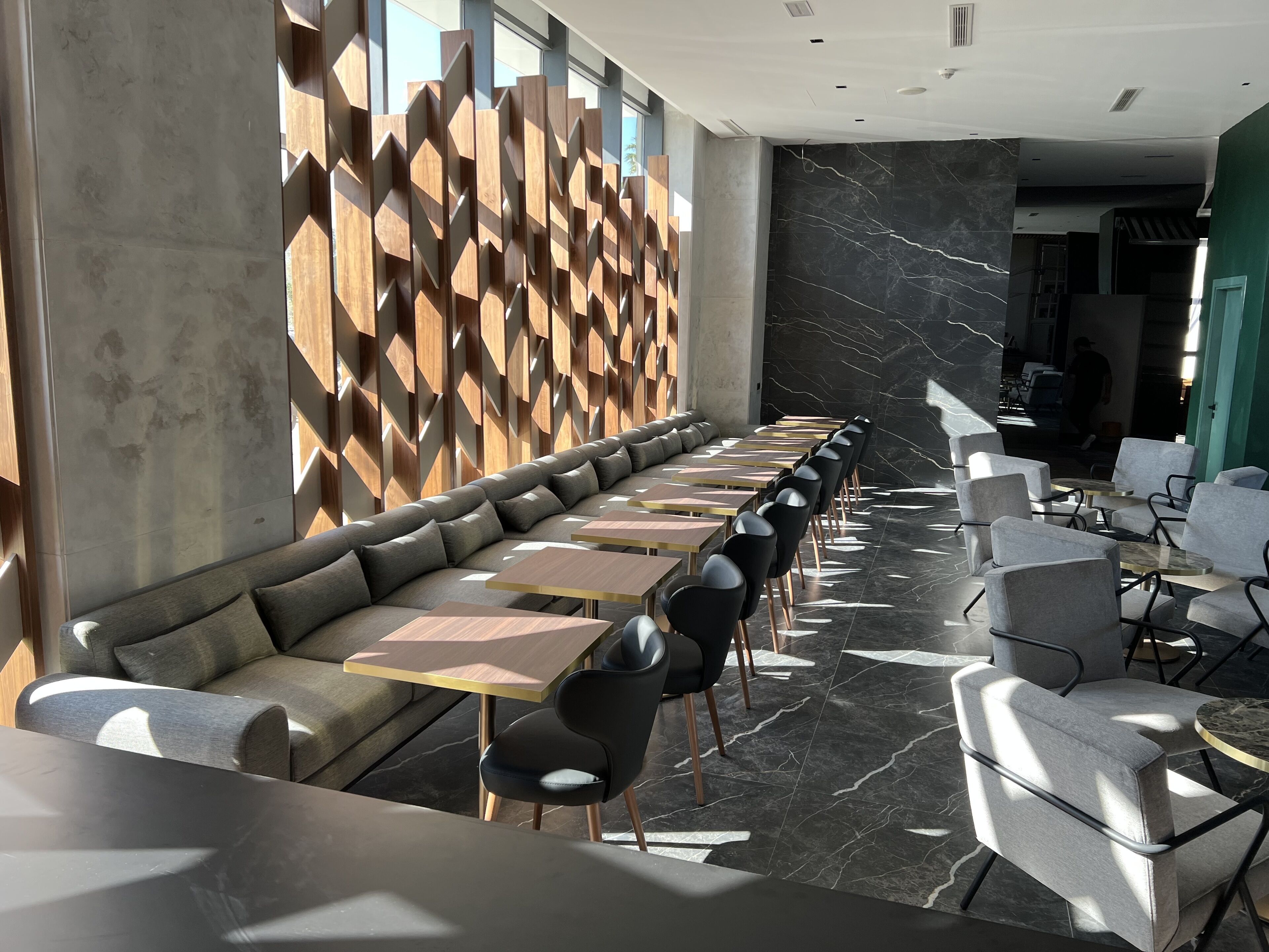 A modern restaurant with a long counter, cushioned seating, and a geometric wall design.