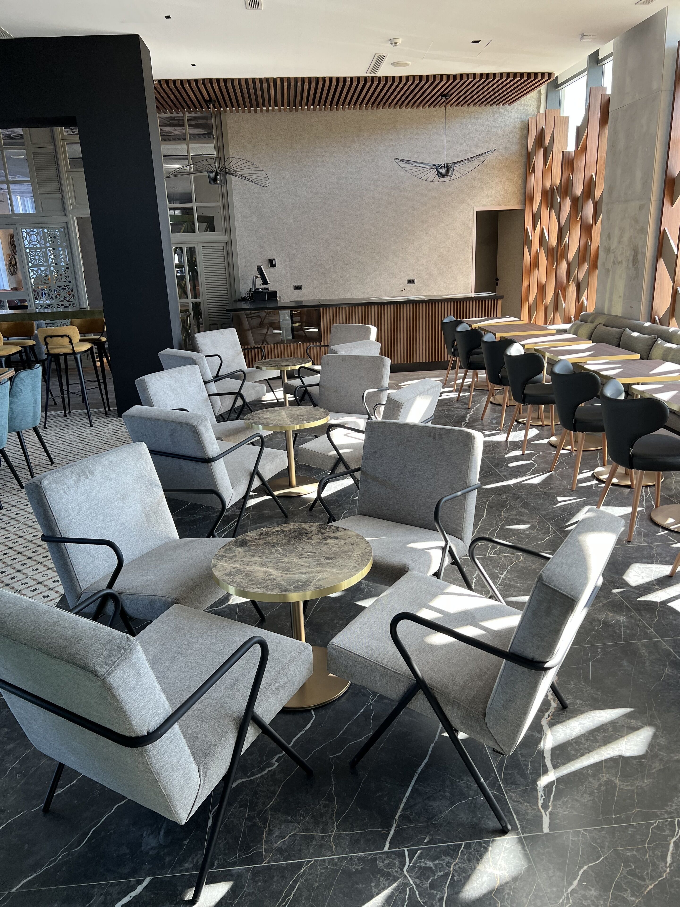 A modern indoor seating area with grey upholstered chairs, round tables, and a patterned wall.