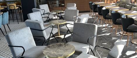A modern indoor seating area with grey upholstered chairs, round tables, and a patterned wall.