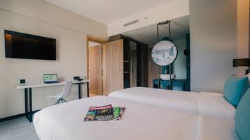 Una habitación de hotel moderna con una cama grande, un escritorio con una computadora portátil, un televisor montado en la pared y un espejo circular.