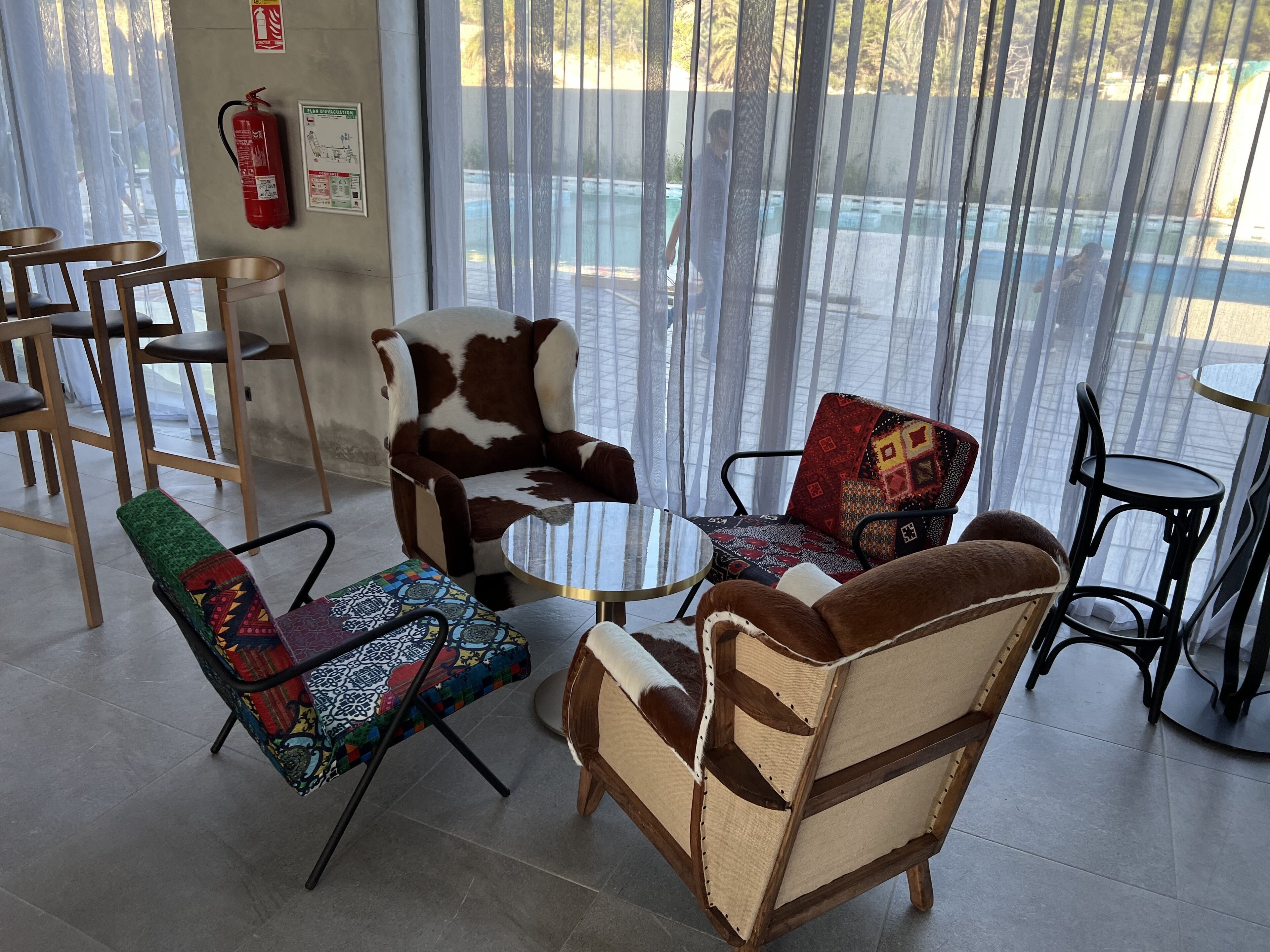 Un interior moderno con una combinación de mobiliario de madera y tapizado, un extintor de incendios y un vidrio que da a un espacio exterior.