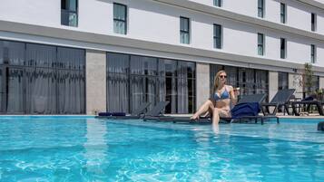 A swimming pool with lounge chairs and a building with multiple windows in the background.
