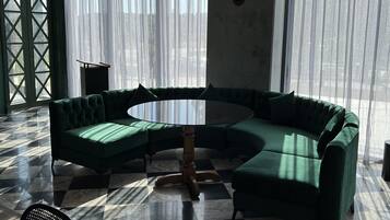 Een ruime kamer met een grote, groene modulaire bank, een ronde tafel en een stierenkop aan de muur.