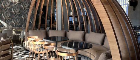 A modern lounge area with a curved wooden structure, seating arrangements, and a patterned floor.