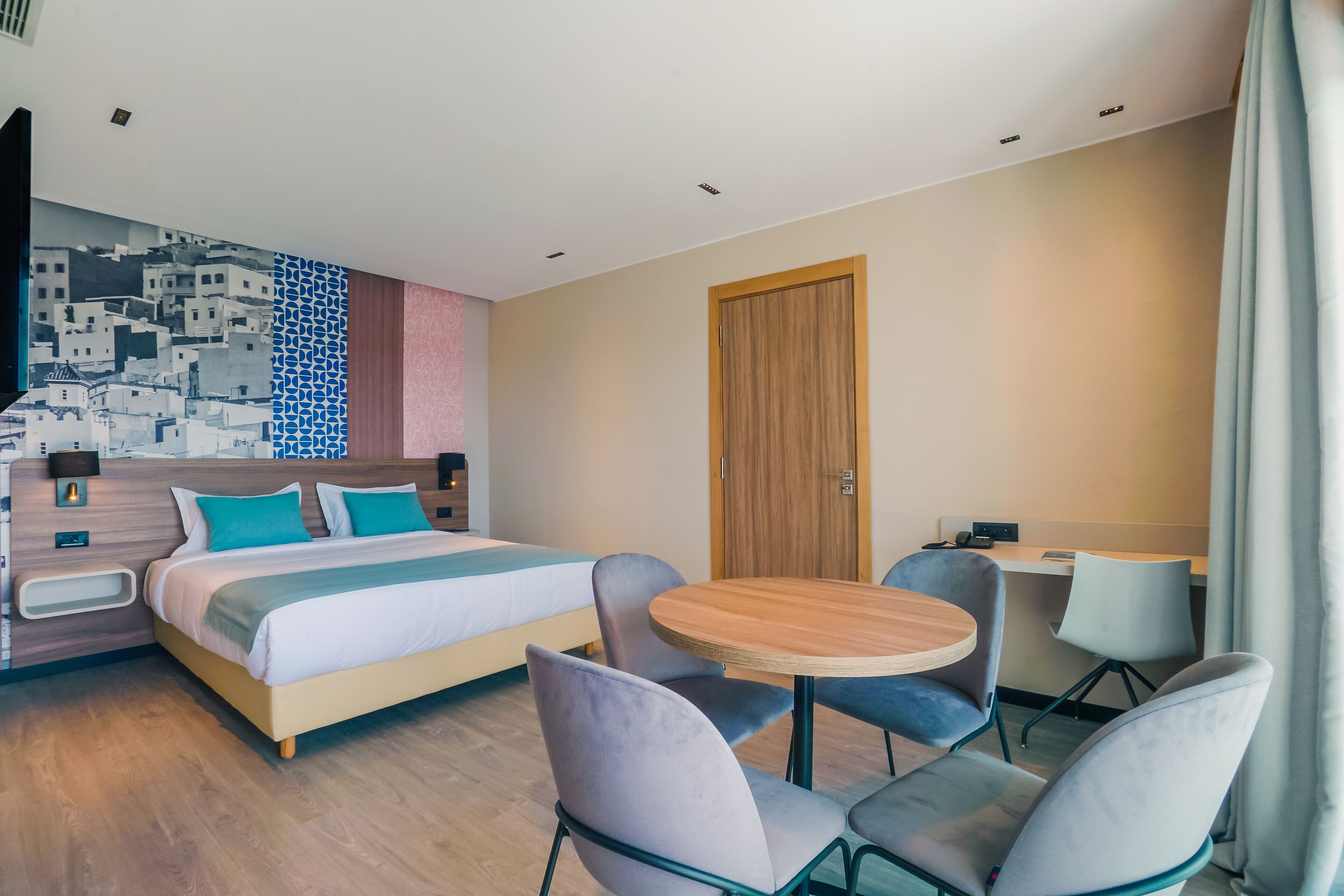 A hotel room with a bed, two chairs, a small round table, a desk, and a wooden door.