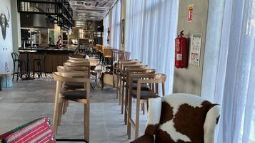 A modern interior with a long corridor leading to a bar area, featuring patterned ceiling, seating with patterned cushions, and a fire extinguisher on the wall.