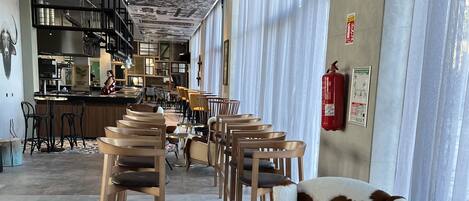 Un interior moderno con un largo pasillo que conduce a una zona de bar, con techo estampado, asientos con cojines estampados y un extintor en la pared.