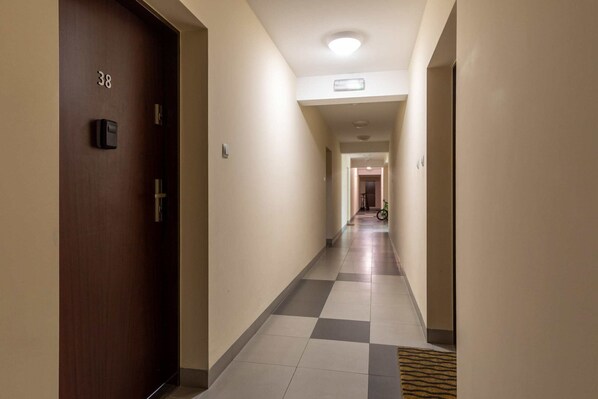 Un pasillo de hotel con piso a cuadros, una puerta de madera con la inscripción '38' y una lámpara en el techo.