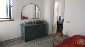Une chambre à coucher comprenant une commode, un miroir, un lit et une porte donnant sur une autre pièce.