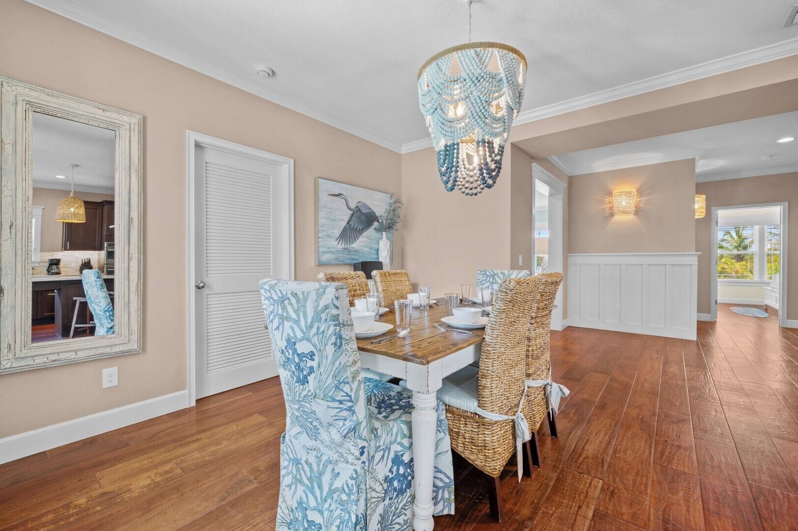 A dining area with a wooden table, wicker chairs, a chandelier, and a large mirror.