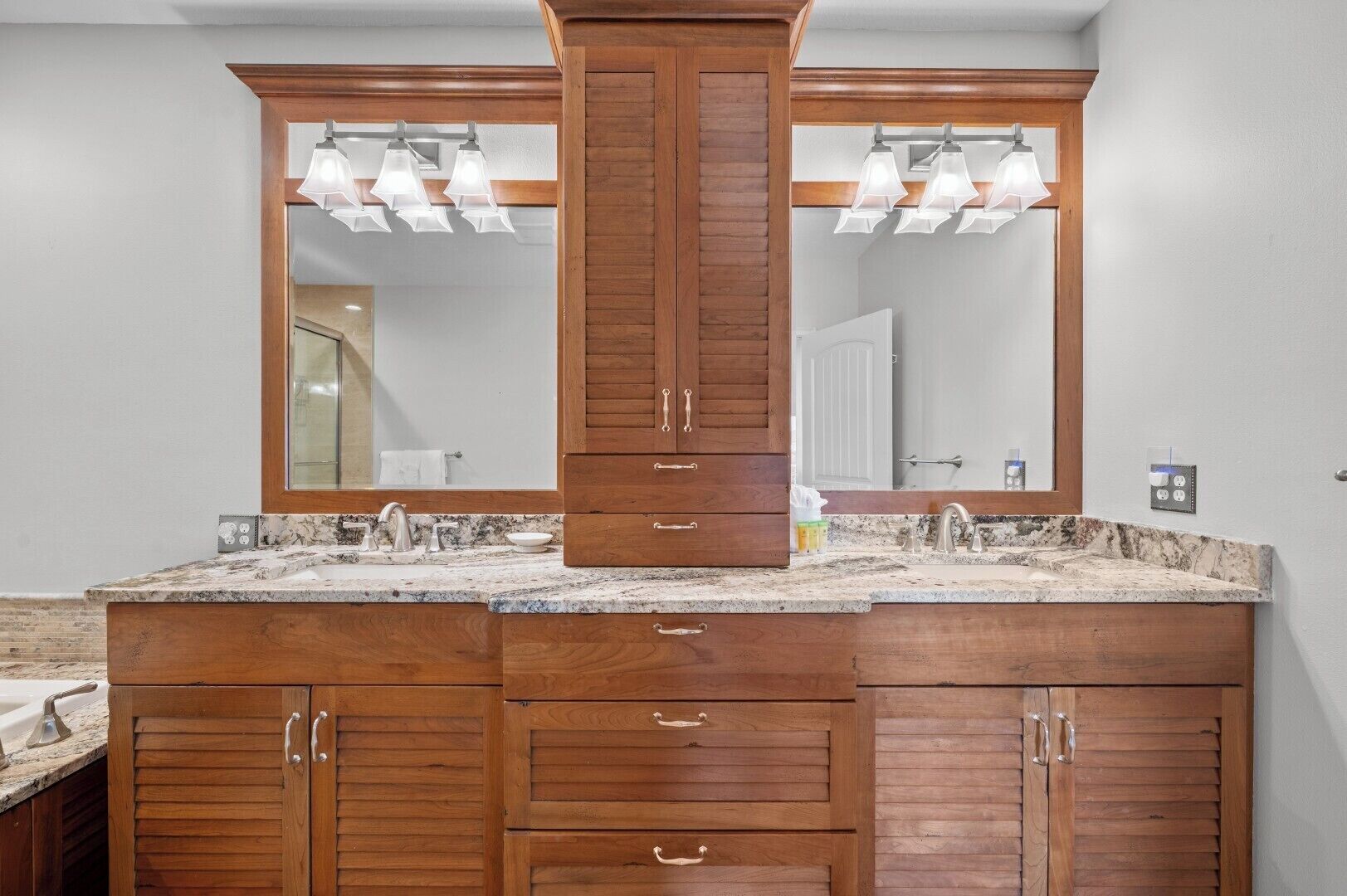 A bathroom with a double vanity, wooden cabinets, a marble countertop, and a large mirror with pendant lights.