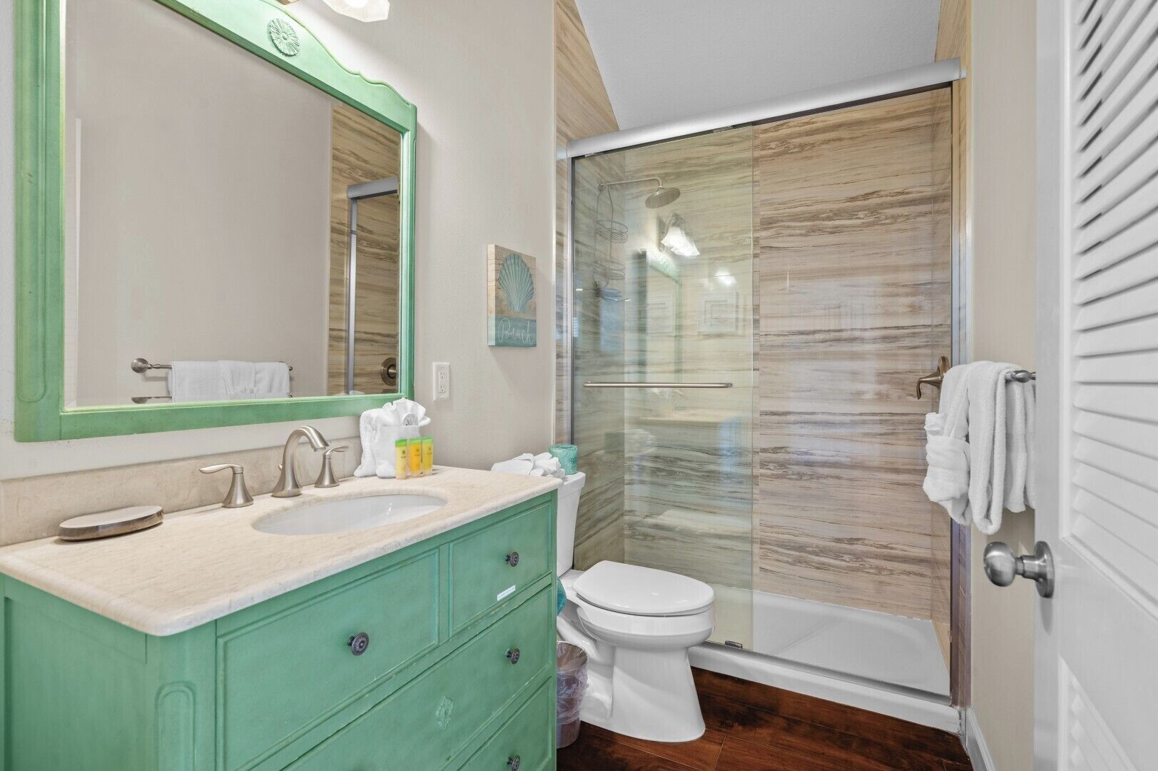 A bathroom with a sink, mirror, toilet, and glass shower enclosure.
