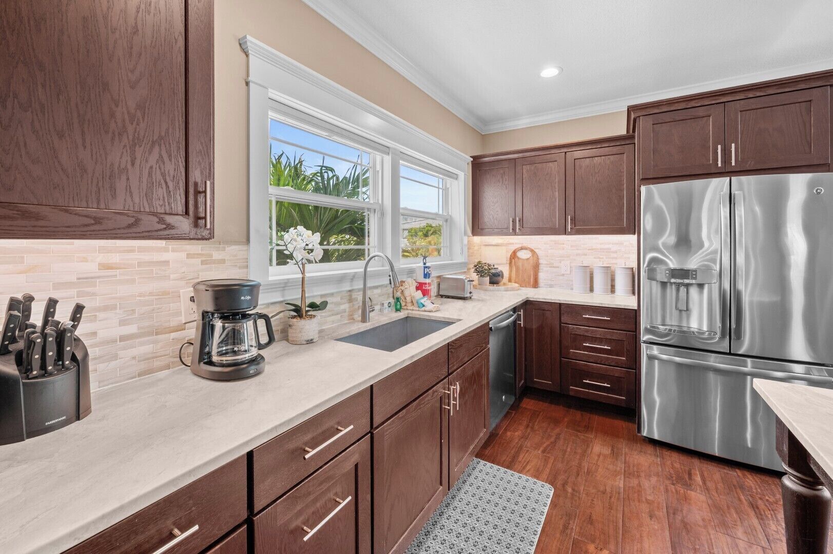 A kitchen with wooden cabinets, a stainless steel refrigerator, a coffee maker, and a window with a view of greenery.