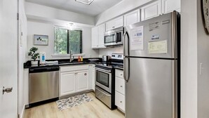 A modern kitchen with stainless steel appliances, white cabinetry, and a window with blinds. - Central Location: Pool, Minutes to Shops & Beach! (Fernandina Beach)