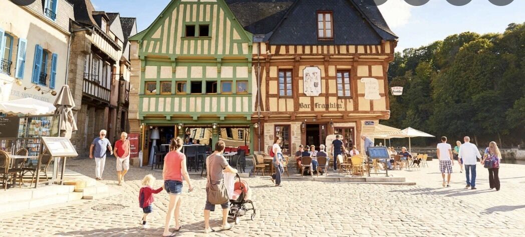 A cobblestone square with traditional half-timbered buildings, outdoor seating, and a few people walking.