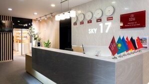 Een hotel receptie met klokken die verschillende tijdzones tonen, een bord met de tekst 'SKY 17' en vlaggen van diverse landen.