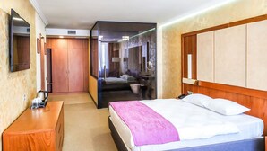 Een hotelkamer met een bed, een houten nachtkastje, een spiegel, een kledingkast en een badkamer zichtbaar door een glazen deur.
