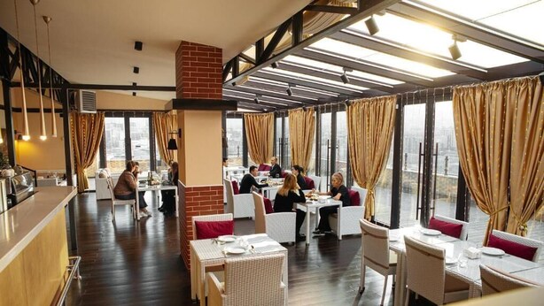 Een restaurant met hoge plafonds, grote ramen en een bar.