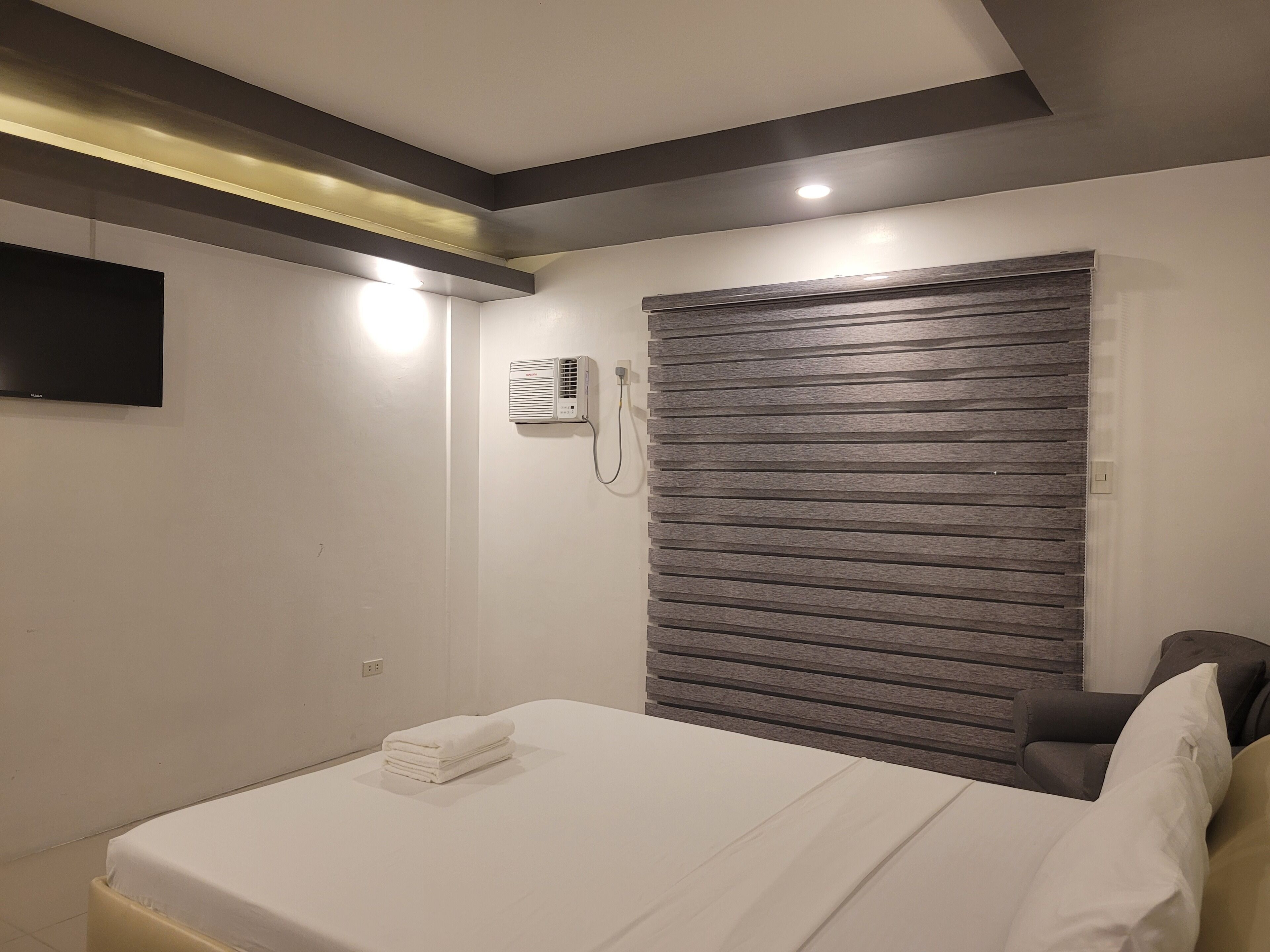 A hotel room with a bed, a wall-mounted air conditioner, and a window with blinds.