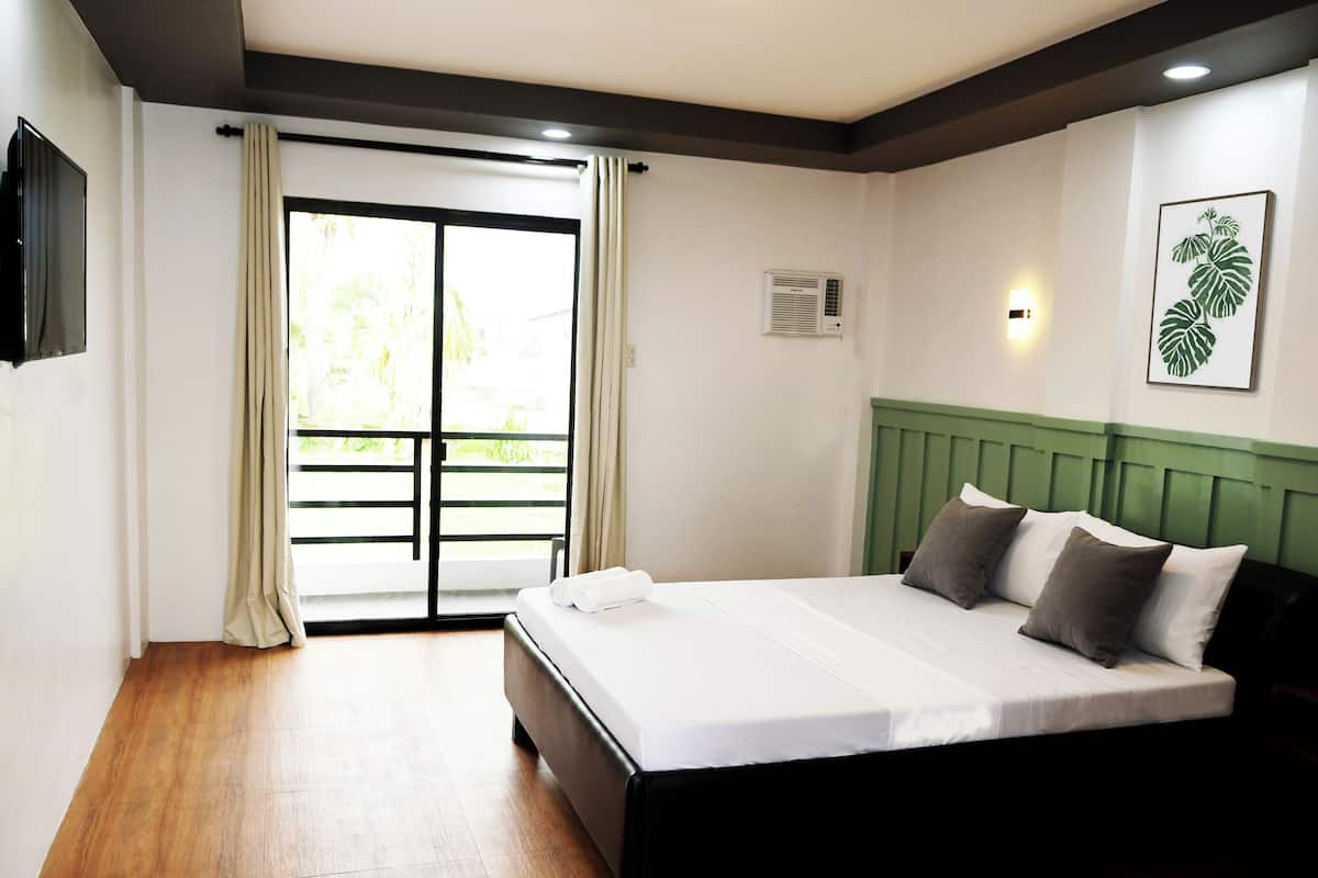 Ein Hotelzimmer mit einem Bett, einer Schiebetür zum Balkon, einem Flachbildfernseher und einer Wand-Klimaanlage.