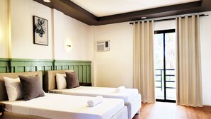 Een hotelkamer met twee bedden, een groen hoofdeinde, een lijst met kunstwerk en een raam met gordijnen.