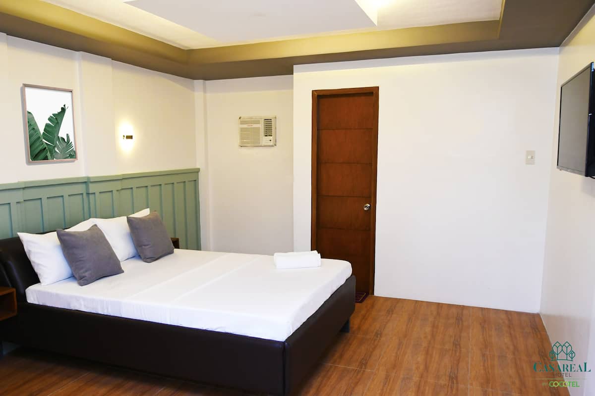 Ein Schlafzimmer mit einem Bett, einem Nachttisch, einer Holztür, einer Wand-Klimaanlage und einem gerahmten Bild.